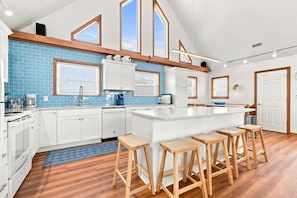 A modern kitchen with white cabinets, a blue-tiled backsplash, wooden stools, and a large island.