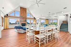 A spacious living area with a high ceiling, a dining table with chairs, a sofa, and a view of the outside.