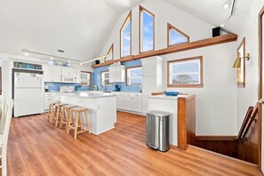 A spacious kitchen with a central island, wooden flooring, and a view of the sky through the windows.