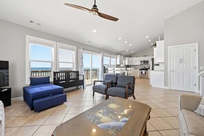 A spacious living area with a balcony, a dining table, and a kitchen in the background.