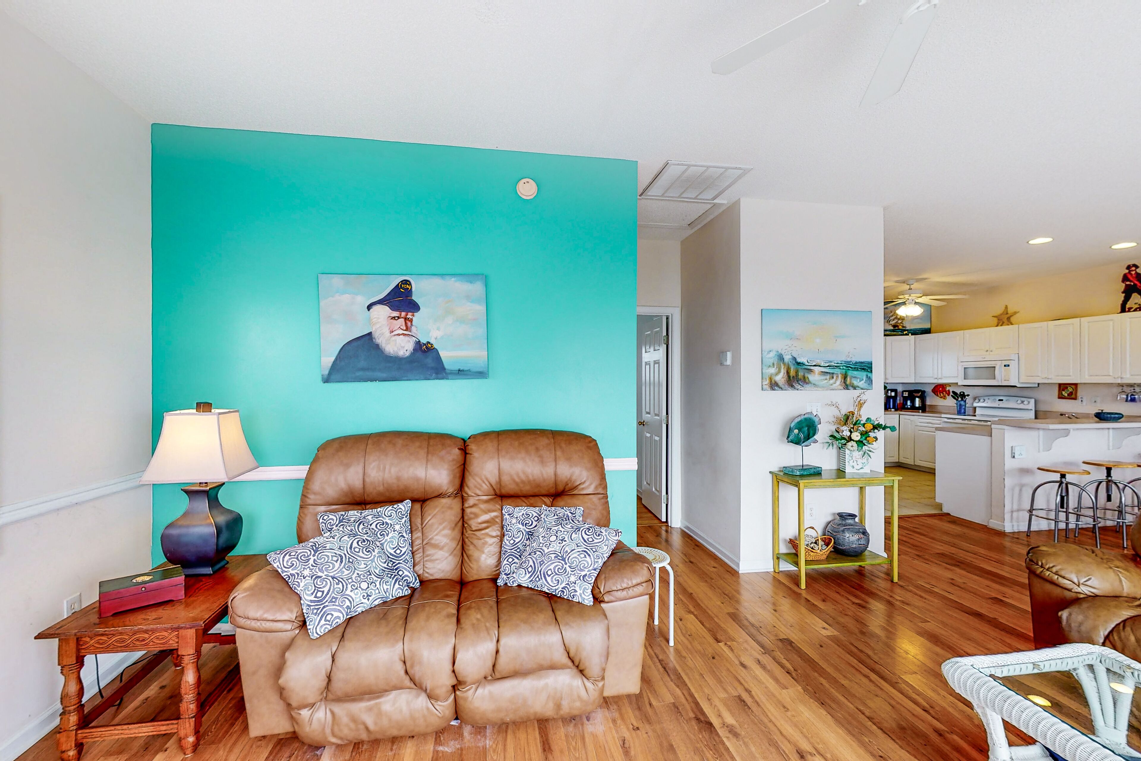 Ein Wohnzimmer mit einer braunen Ledersofa, einer Wand in Türkis und einem Gemälde eines Mannes mit Hut.