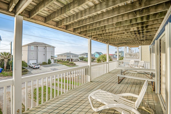 A covered porch with white railings, a wooden deck, and outdoor furniture.