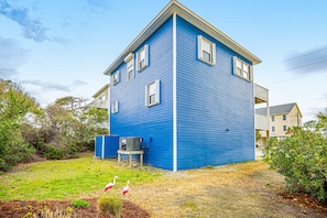 A two-story blue house with a small porch and a single-story building in the background.