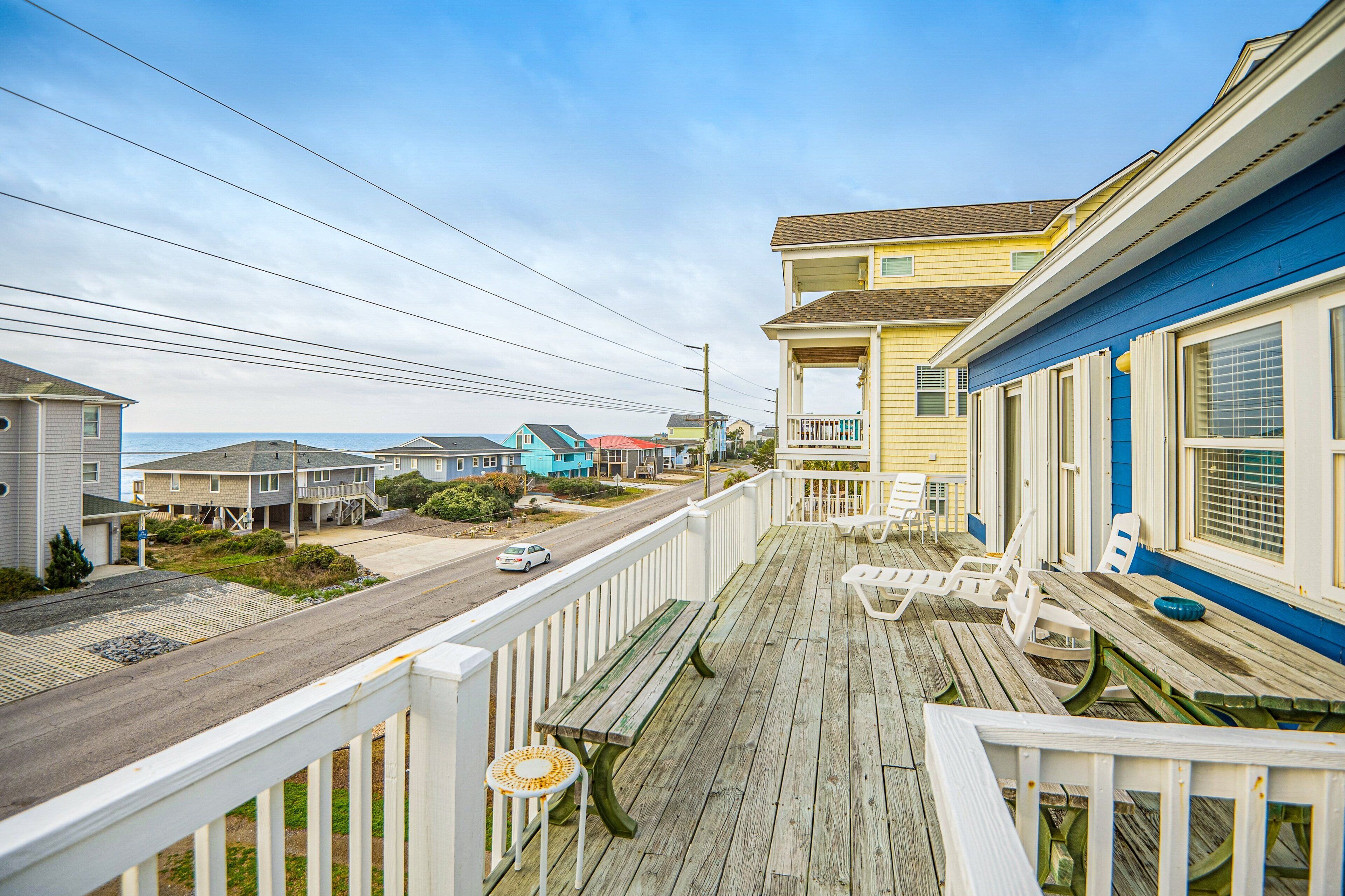 A wooden deck with a bench and chairs, overlooking a street with houses and a road.