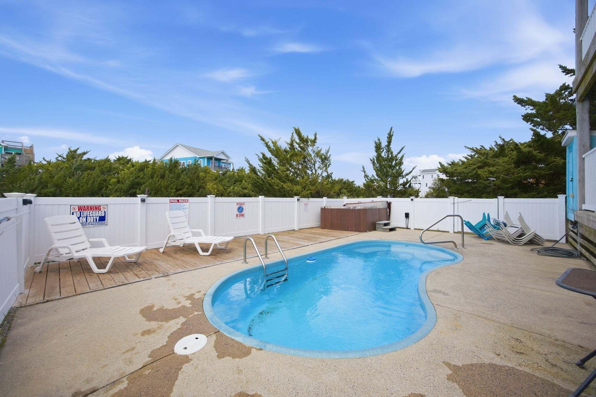 A swimming pool with lounge chairs, a lifeguard duty sign, and a fenced area.