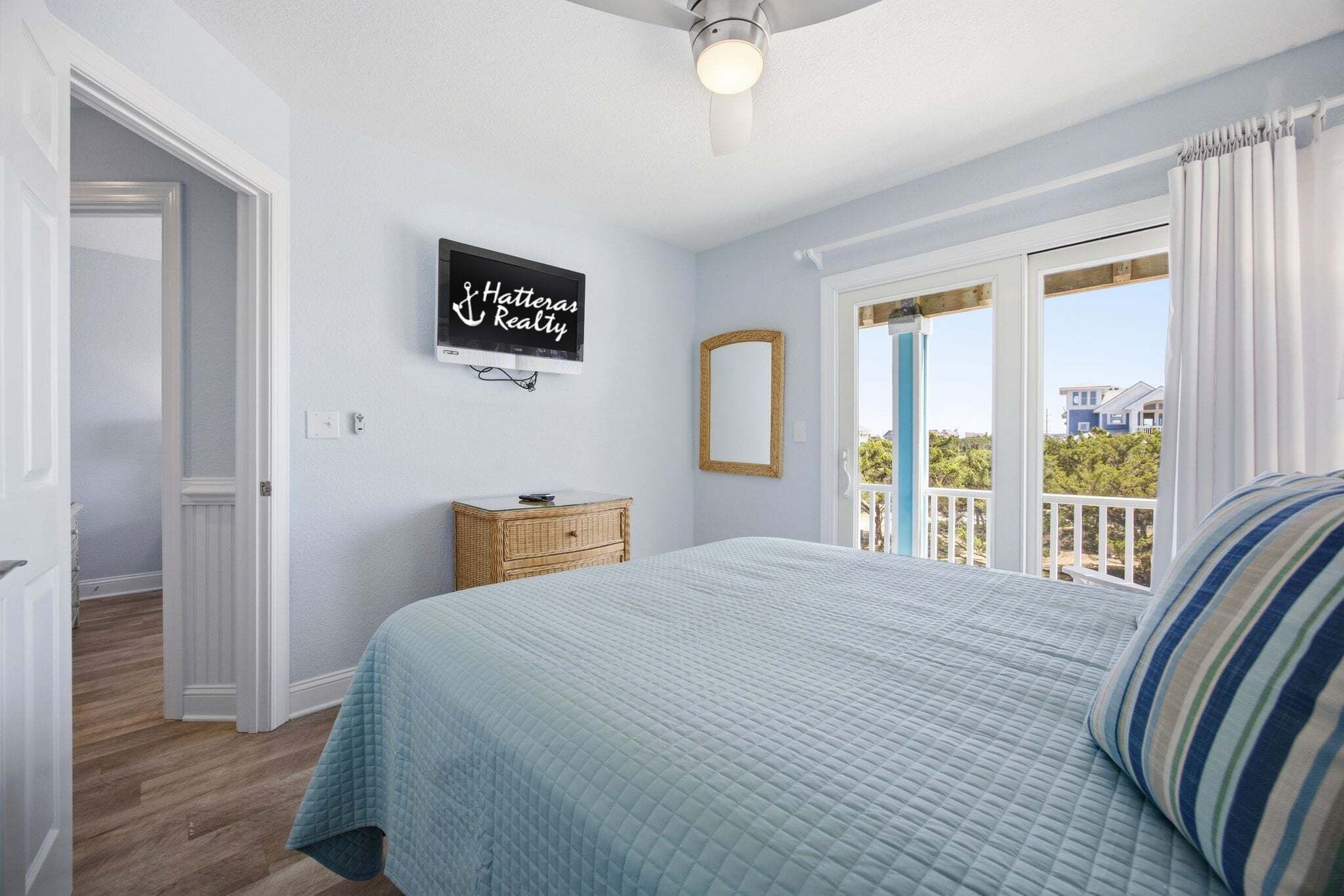 A bedroom with a bed, a television, a dresser, a mirror, and a balcony with a view.