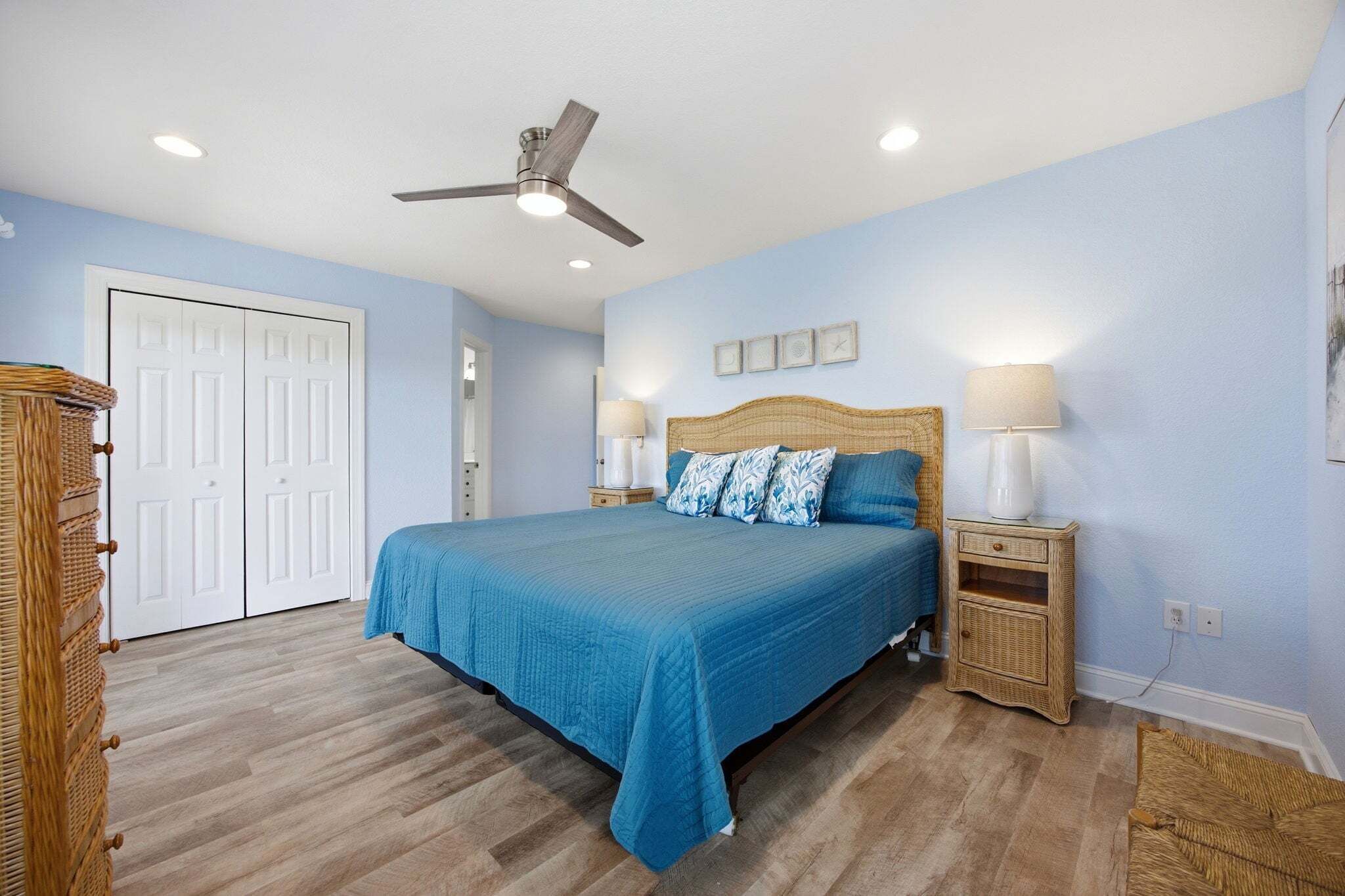 A bedroom with a bed, nightstands, a ceiling fan, and a door.
