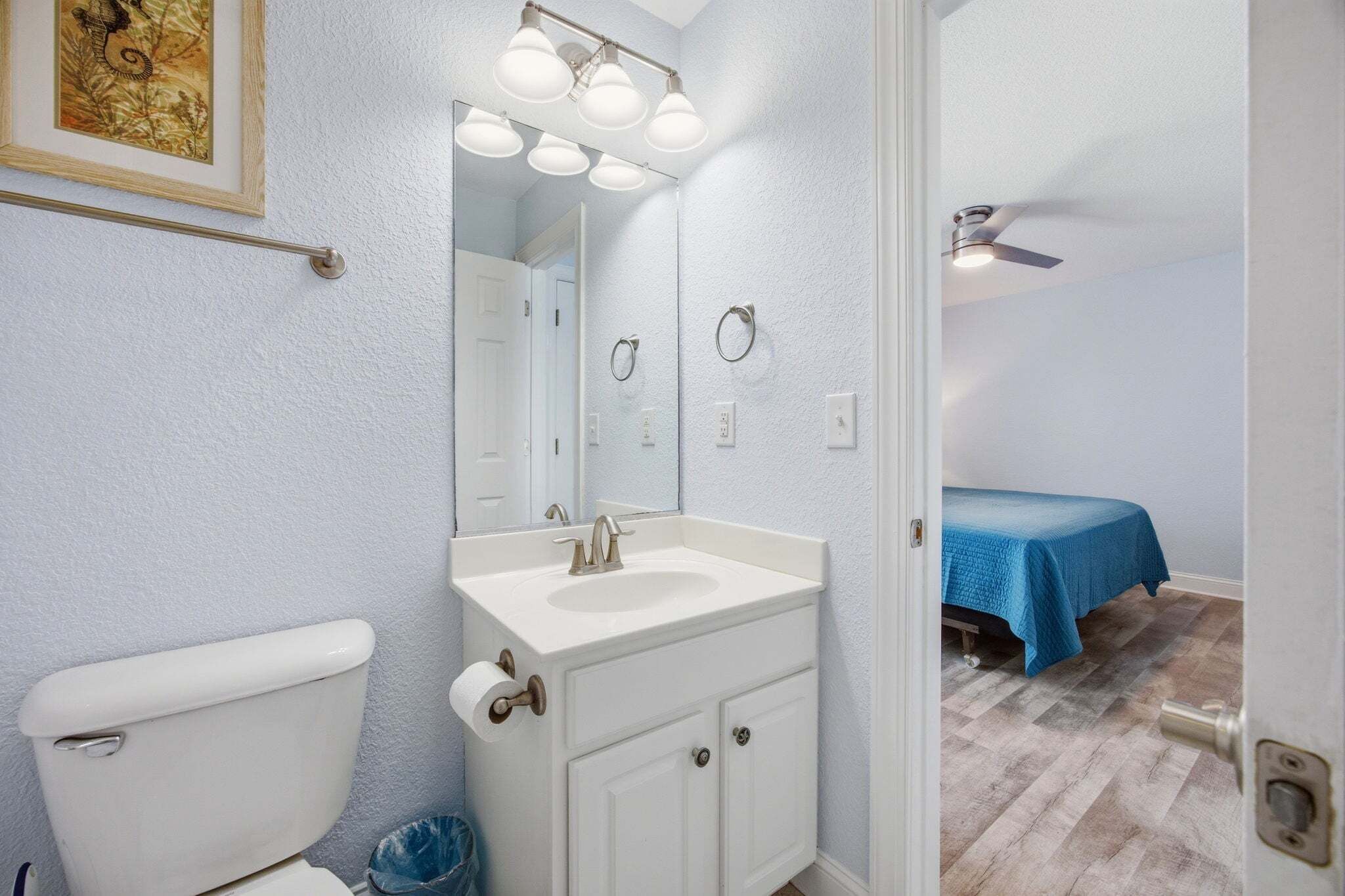 Een badkamer met toilet, wastafel, spiegel en plafondventilator.
