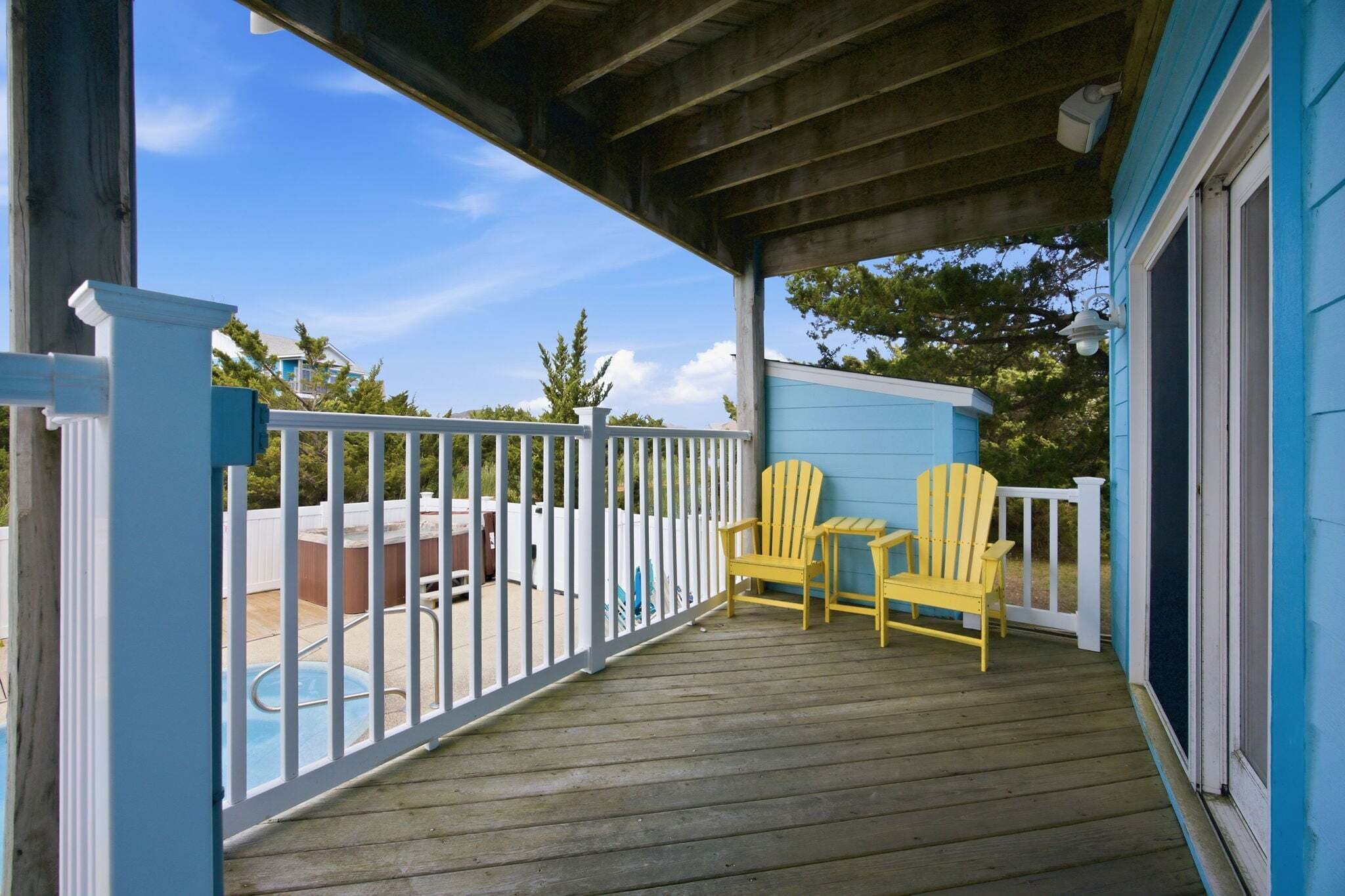 A covered porch with a pool, two yellow Adirondack chairs, and a blue building.