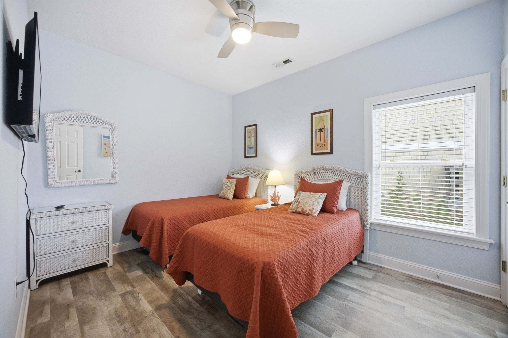 Une chambre avec deux lits, un ventilateur de plafond, une commode, un téléviseur et une fenêtre avec des stores.