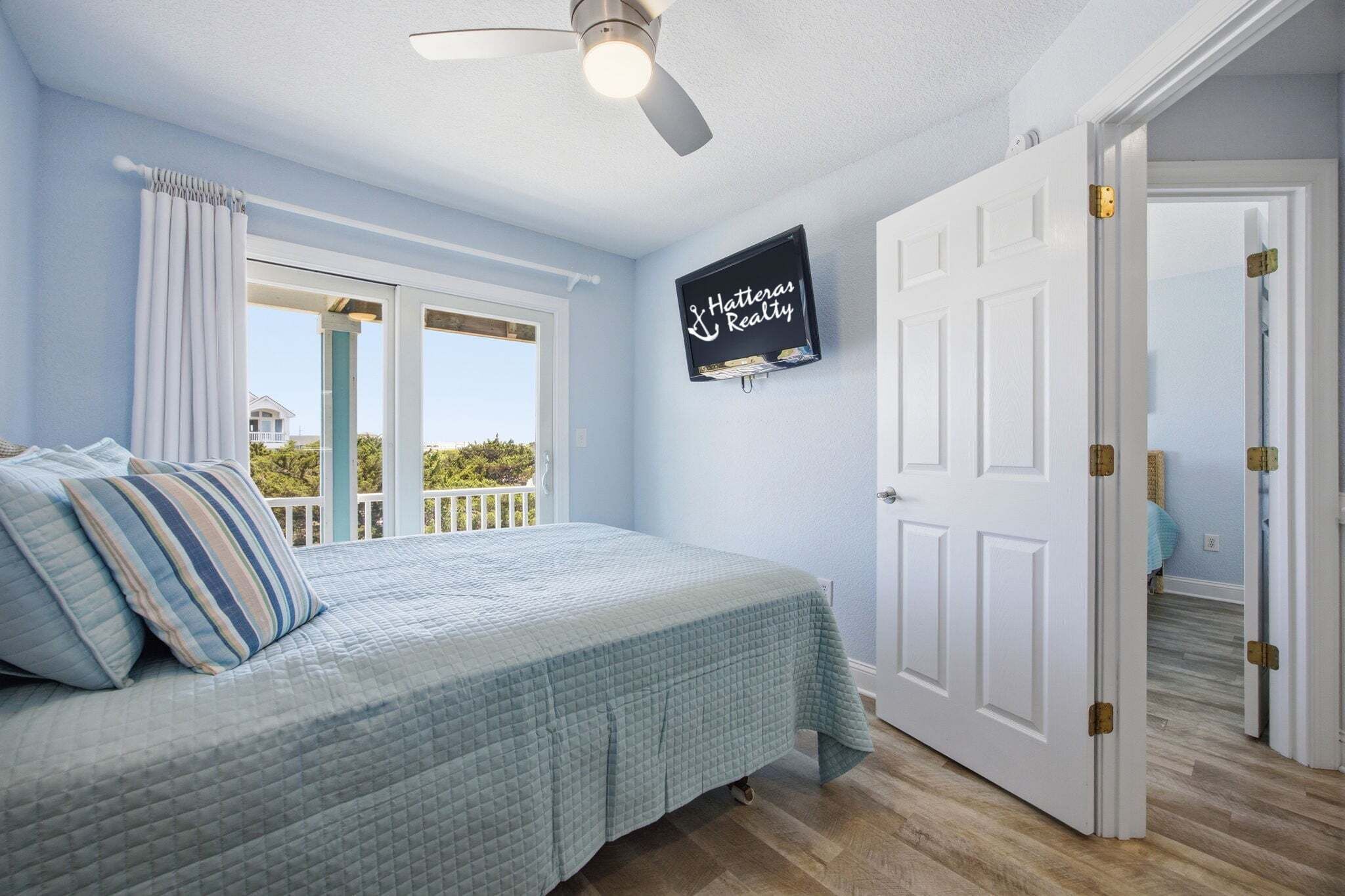 A bedroom with a bed, a ceiling fan, a window with curtains, and a door with a sign.