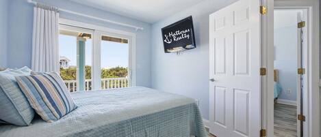 A bedroom with a bed, a ceiling fan, a window with curtains, and a door with a sign.