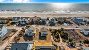 A coastal residential area with houses, a beach, and a clear sky. - Large and roomy house across from the beach with WiFi, W/D, central AC, and deck (Holden Beach)
