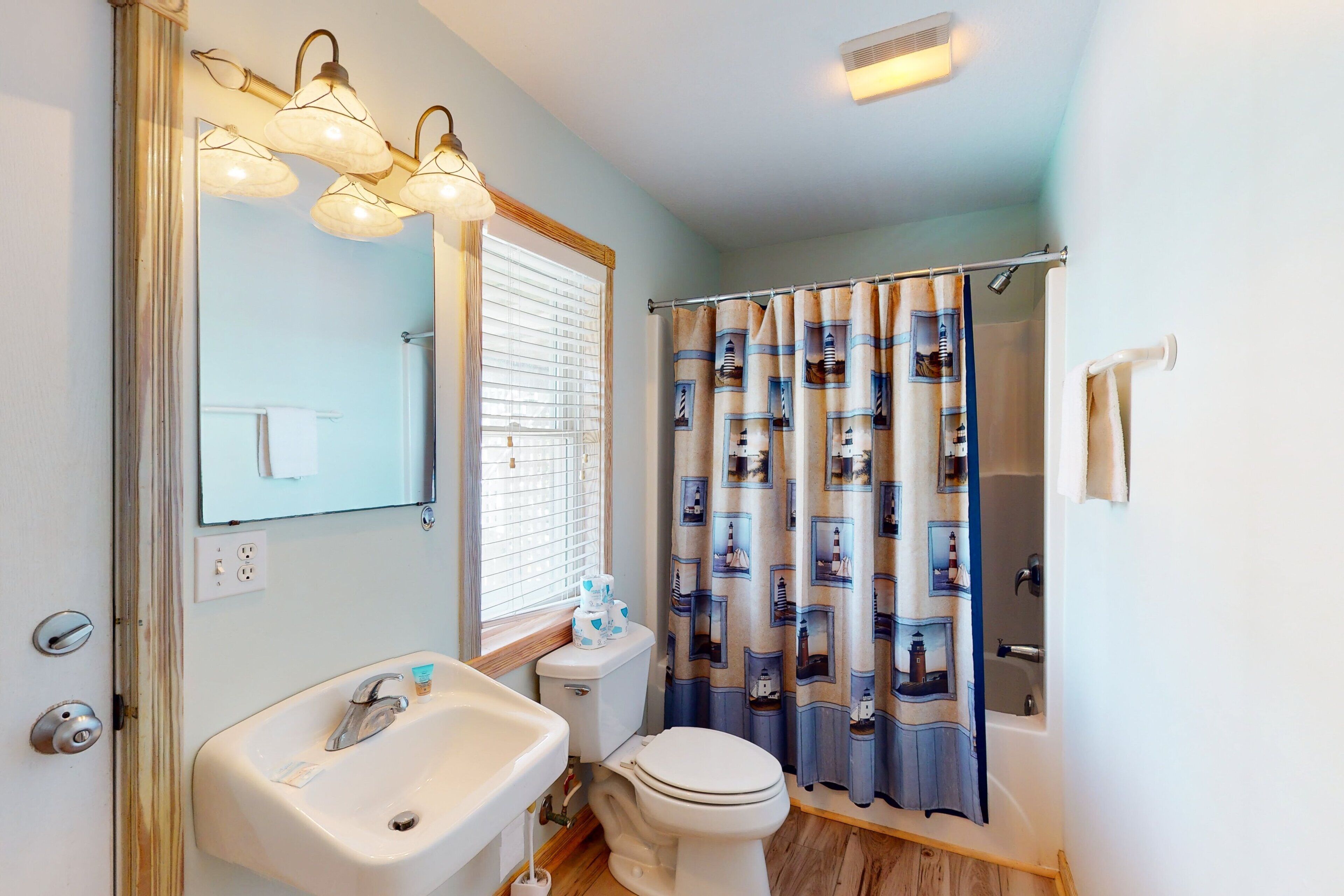 A bathroom with a sink, toilet, and shower curtain with nautical designs.