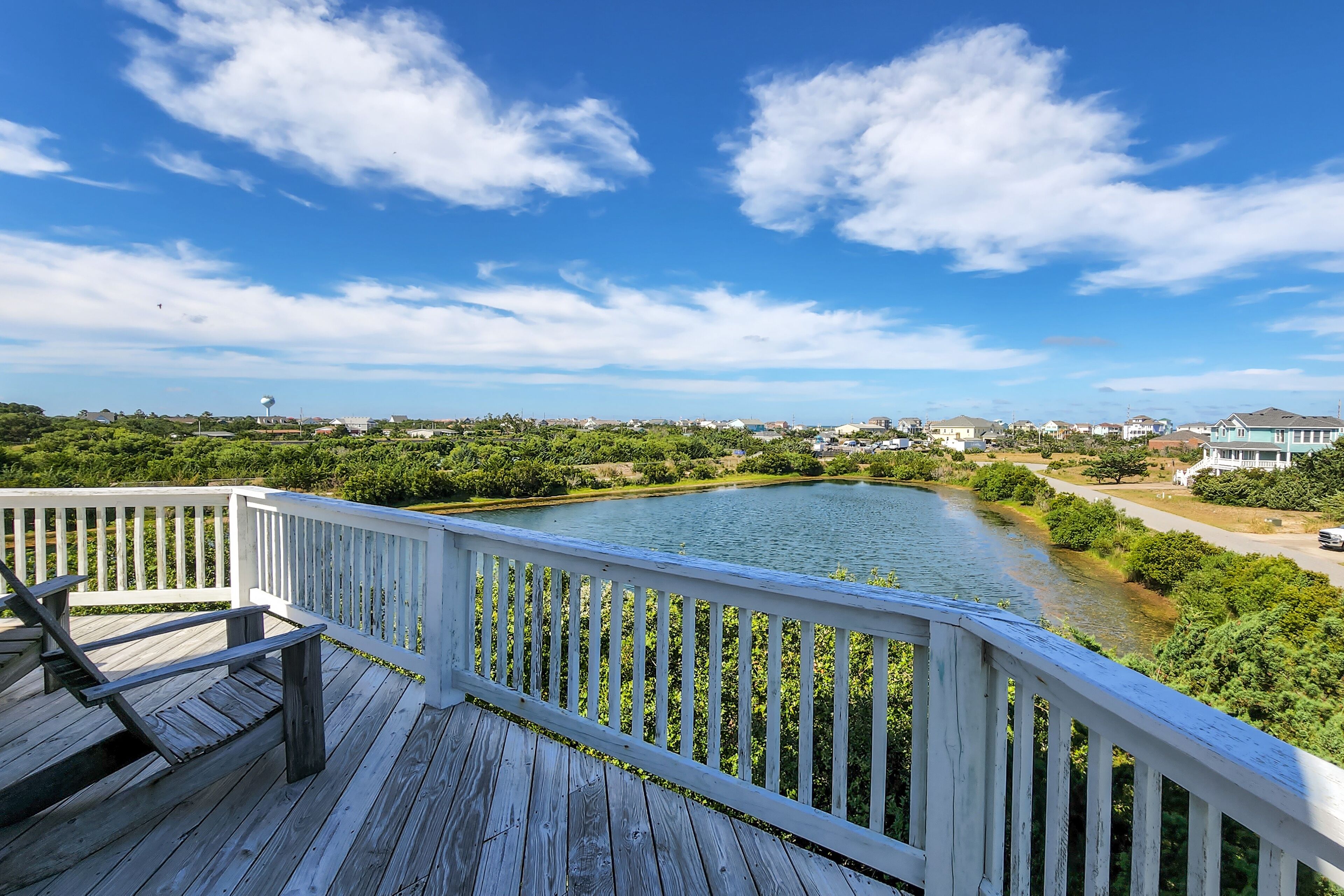 A wooden deck with white railings overlooking a river and greenery.