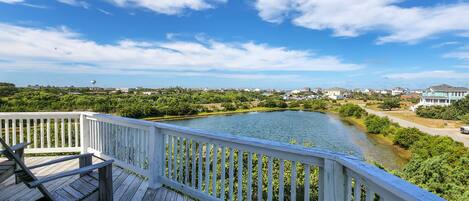 A wooden deck with white railings overlooking a river and greenery.