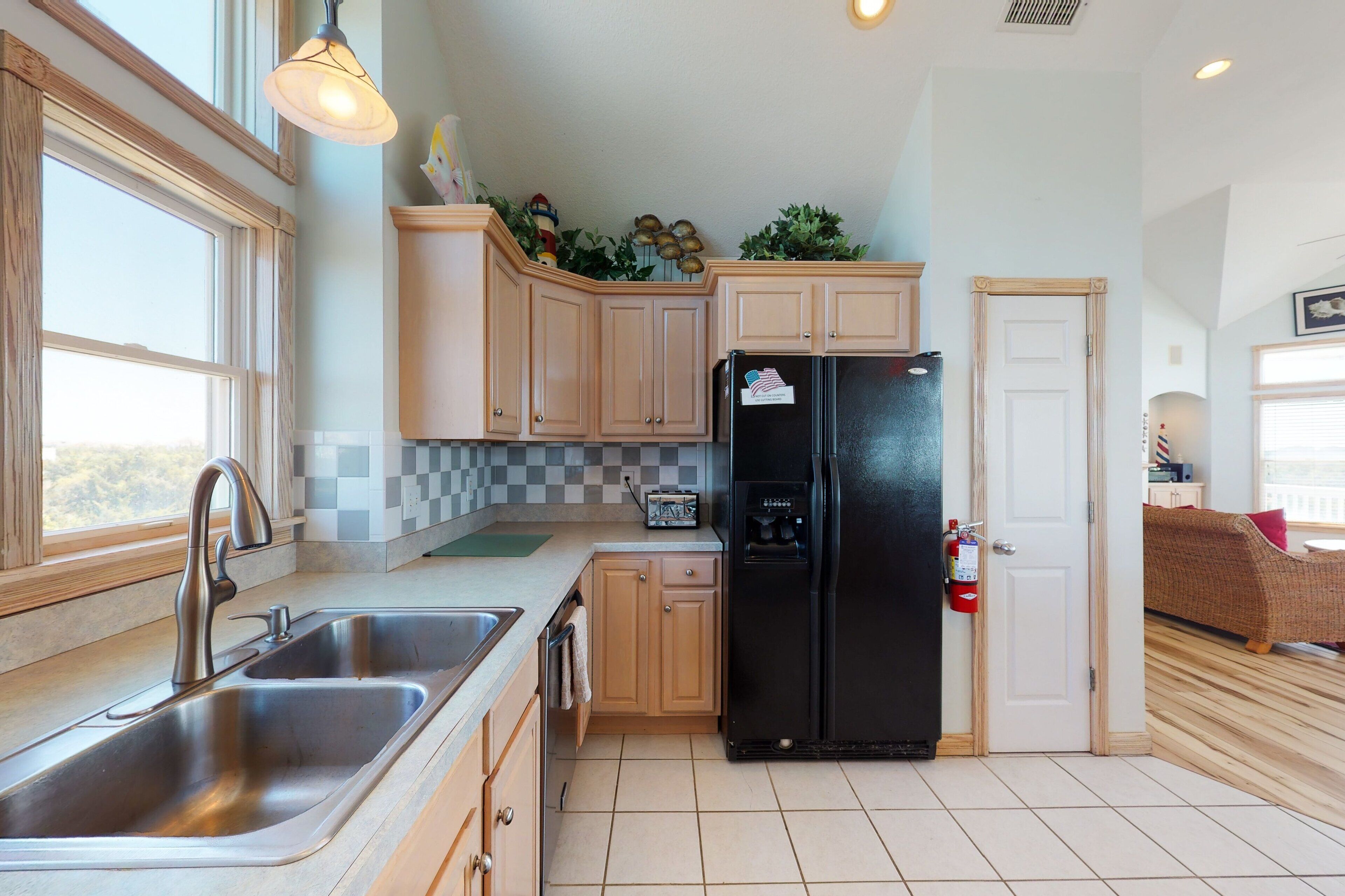 A kitchen with a stainless steel sink, wooden cabinets, a black refrigerator, and a window providing natural light.