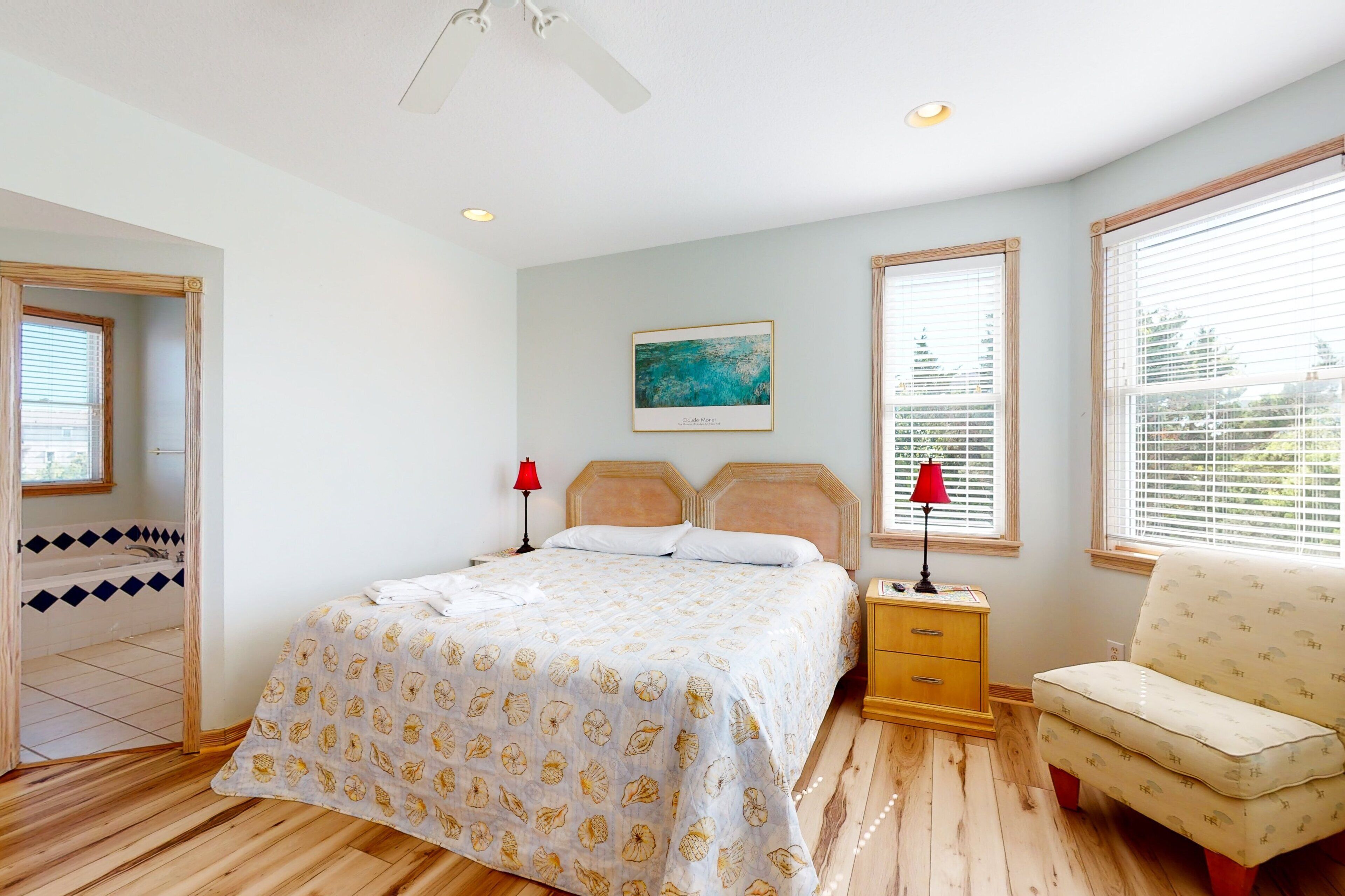A bedroom with a bed, bedside lamps, a chair, a window, and a painting on the wall.