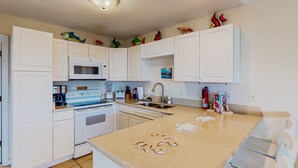 A kitchen with white cabinets, a microwave, a stove, and a sink. There are decorative fish on the cabinets and a fire extinguisher on the wall. - Dog-friendly duplex in Surf City with beautiful ocean views — just steps from beach access! (Surf City)