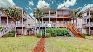A beachfront hotel with multiple balconies, a central staircase, and a palm tree. - Dog-friendly duplex in Surf City with beautiful ocean views — just steps from beach access! (Surf City)