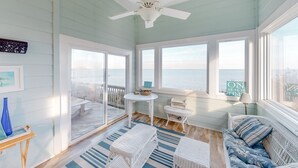 A room with a view of the ocean, a ceiling fan, a wicker sofa, and a small table with a lamp. - Waterfront house with private pool, hot tub, W/D, &vocean view (Buxton)
