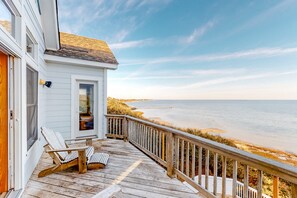A wooden deck with a white house, a chair, and a view of the ocean. - Waterfront house with private pool, hot tub, W/D, &vocean view (Buxton)