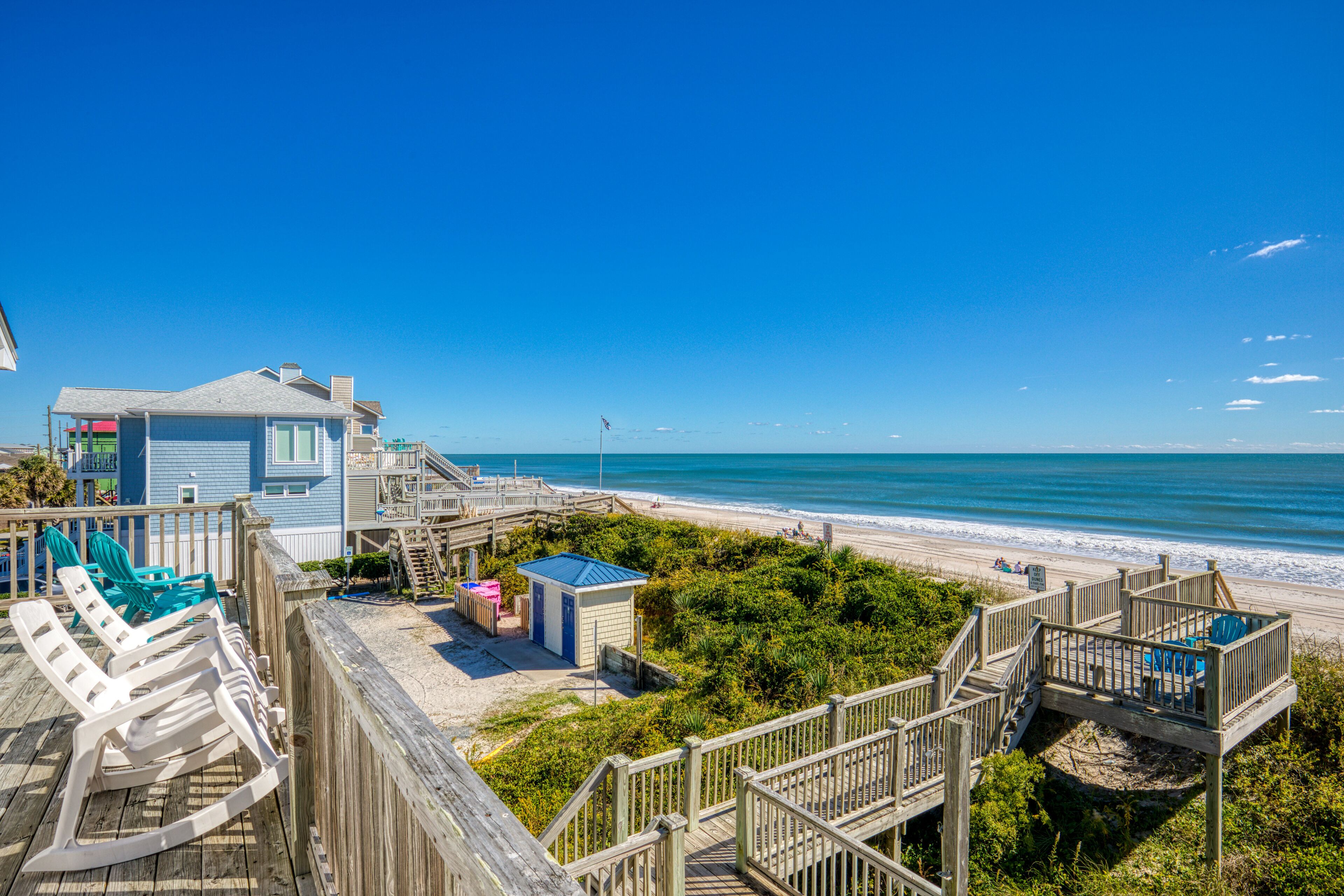 A beachside property with a wooden deck, lounge chairs, and a small building with a blue roof.