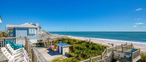 A beachside property with a wooden deck, lounge chairs, and a small building with a blue roof.
