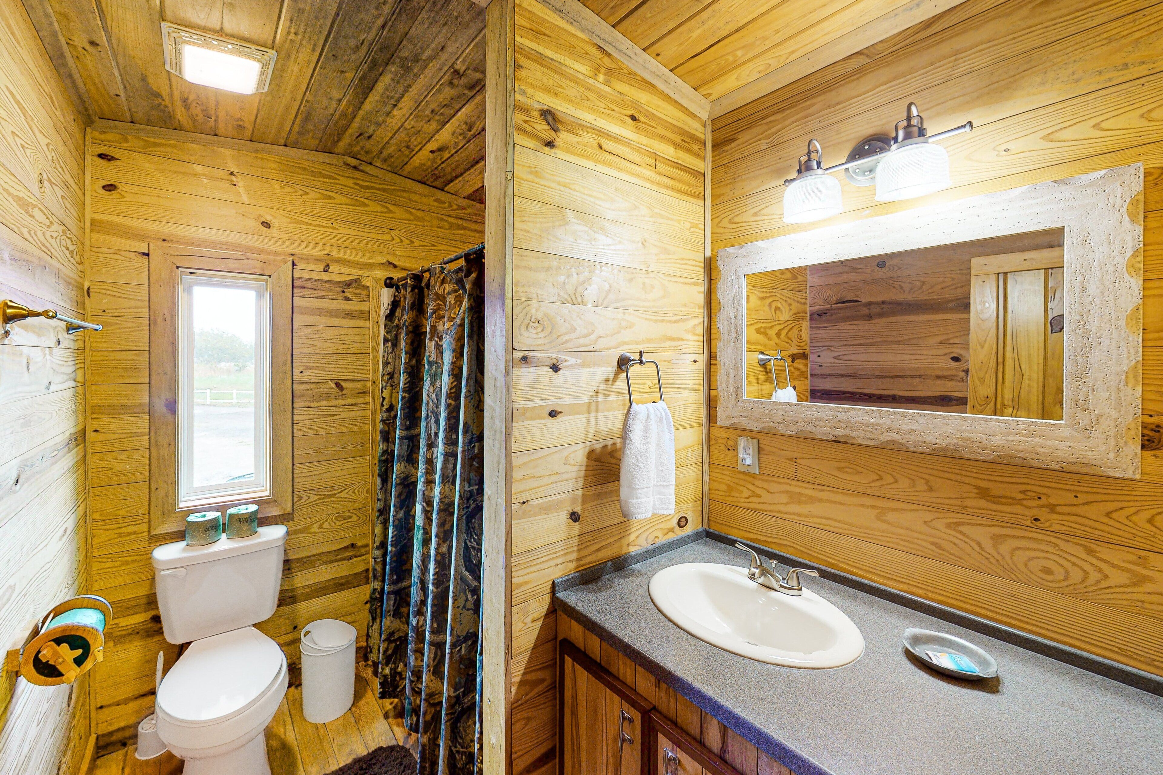 A wooden cabin bathroom with a toilet, sink, and window.