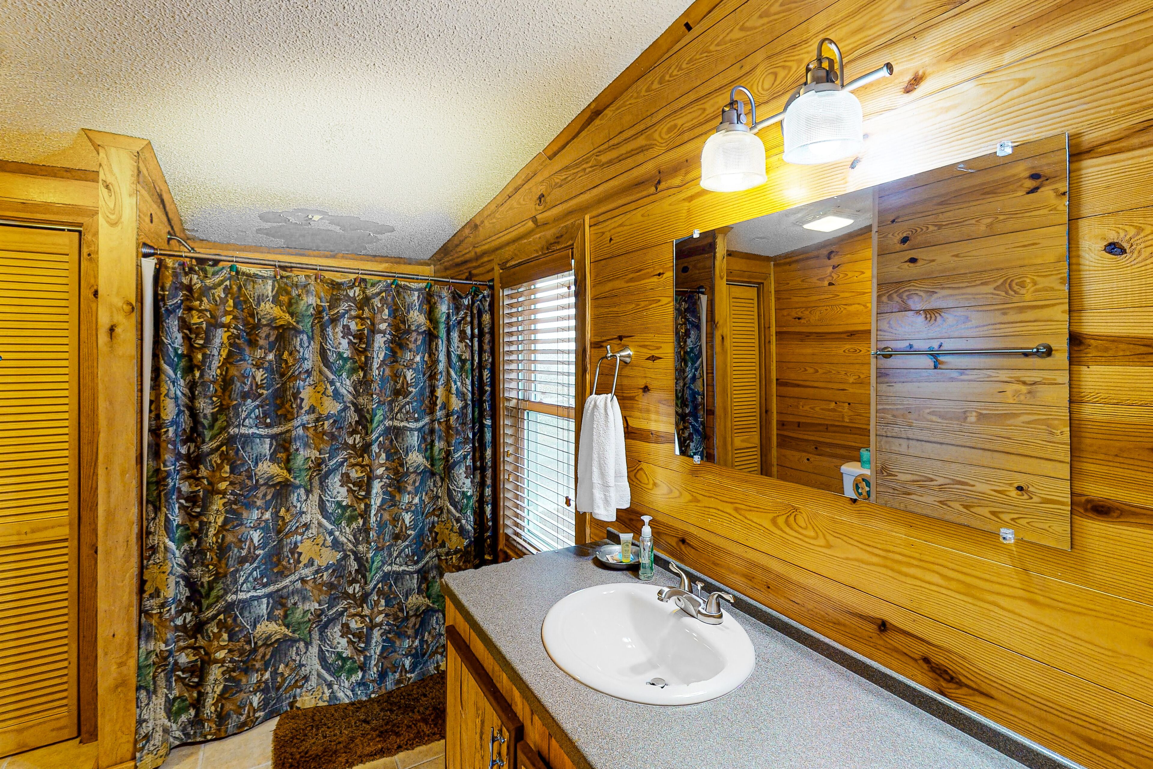 Un baño de cabaña de madera con un espejo grande, un lavabo y una cortina de ducha estampada con hojas.