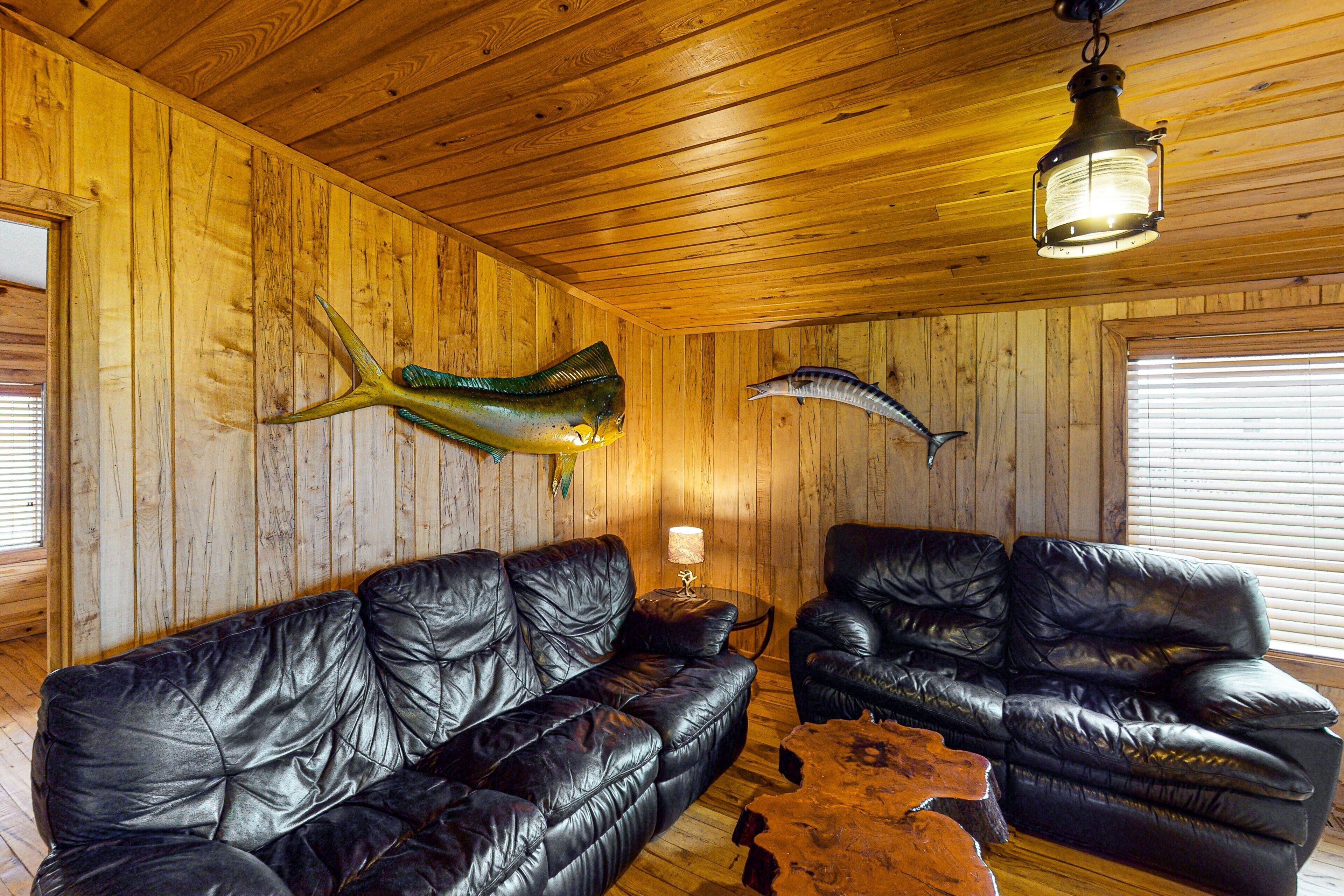 A wooden interior with two black leather sofas, a wooden coffee table, and a hanging lantern.