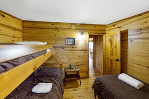 A cabin with wooden walls, a bunk bed, a small table, and a door leading to another room.