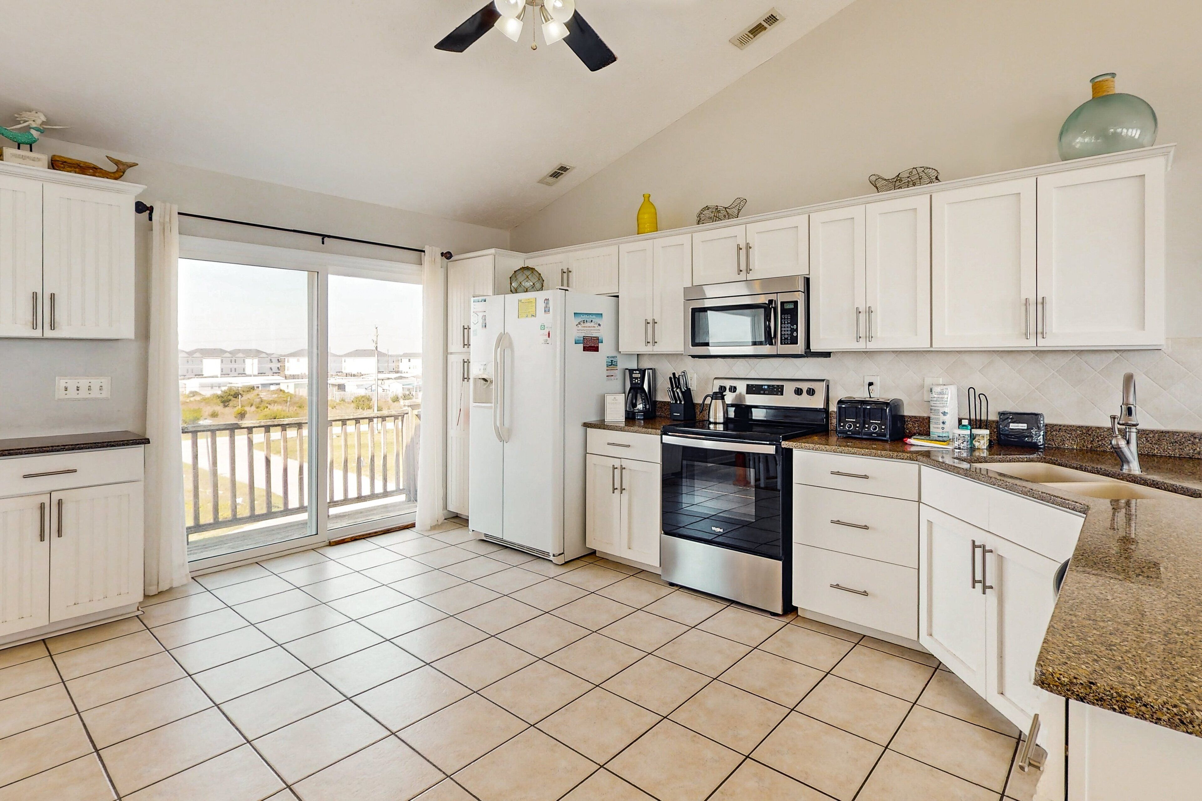 A modern kitchen with white cabinets, a stainless steel oven, a microwave, and a large window overlooking a balcony.