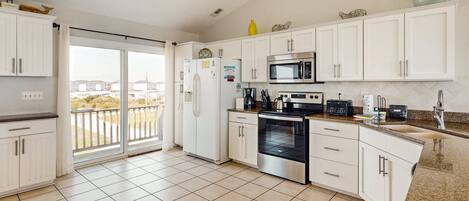 A modern kitchen with white cabinets, a stainless steel oven, a microwave, and a large window overlooking a balcony.