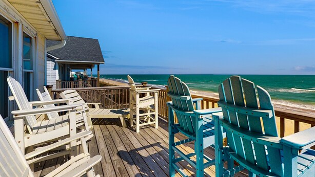 Een houten terras met Adirondack-stoelen met uitzicht op de oceaan.