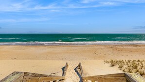 Een houten looppad dat naar een zandstrand leidt, met golven op de achtergrond.