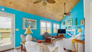 A spacious living room with a wooden ceiling, large windows, and a view of the outdoors. - HB93 Holden Friends - 2nd row, 3 bedroom, NEW private pool (Holden Beach)