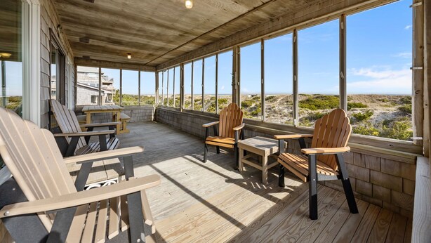 Un espace extérieur abrité, doté de mobilier en bois, de grandes fenêtres et offrant une vue sur le paysage.