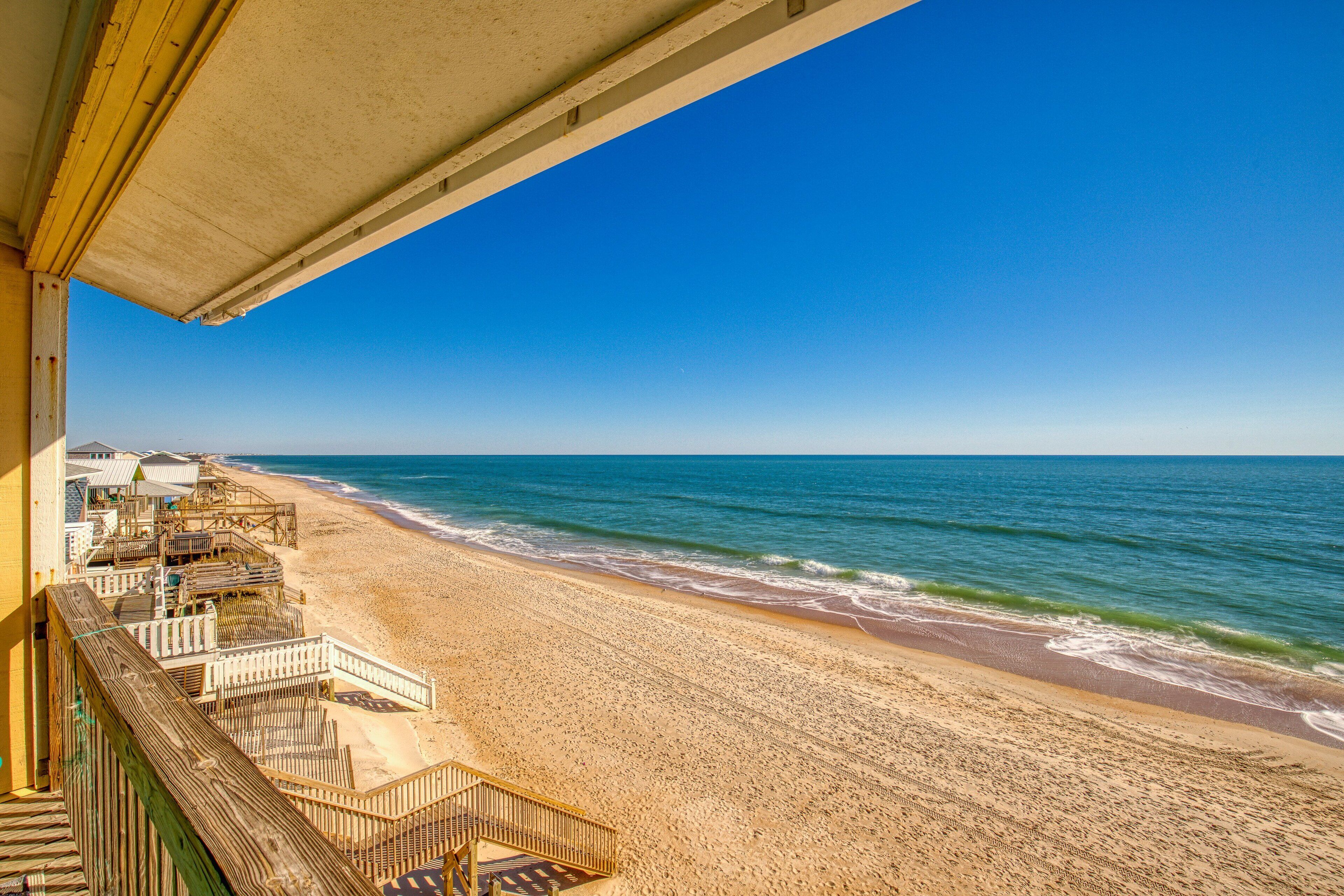 Ein Strand mit einer hölzernen Promenade, die zu einem Gebäude mit einem Balkon mit Blick aufs Meer führt.