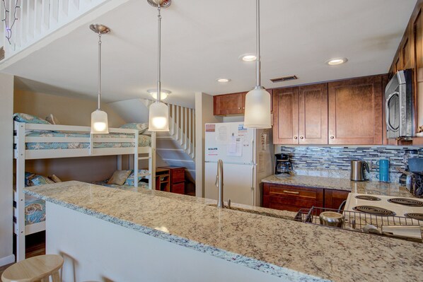 A kitchen with granite countertops, wooden cabinets, a stainless steel refrigerator, and a microwave. - Oceanfront condo with unlimited beach views, private beach access, community pool and more..! (Surf City)