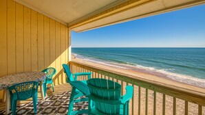 A wooden deck with a table and chairs overlooking a beach. - Oceanfront condo with beach views, balcony, community pool & W/D, central AC (Surf City)