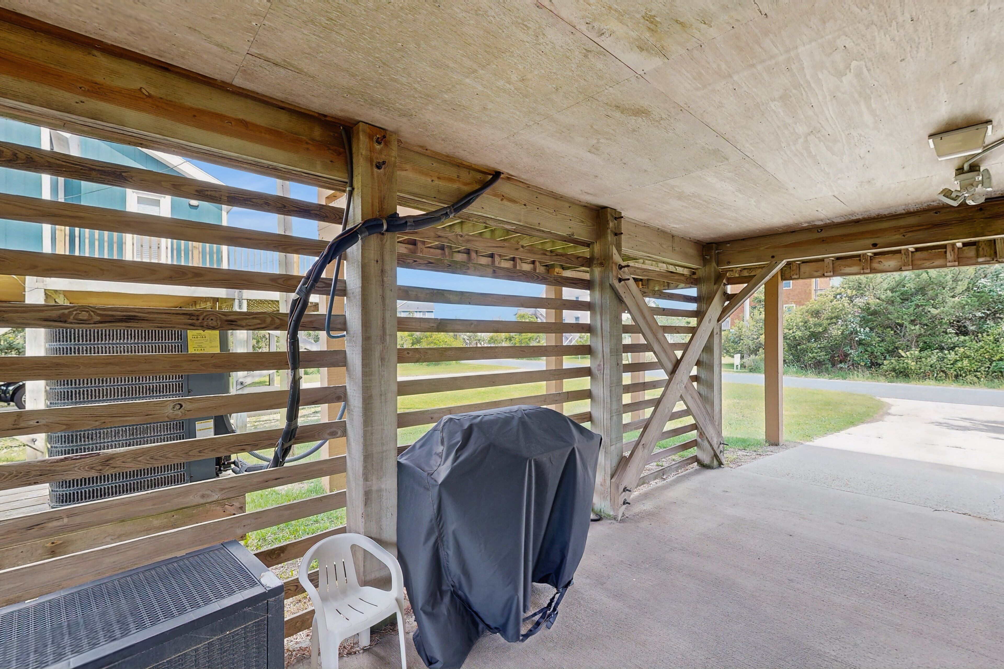 A covered outdoor area with a grill, a white plastic chair, and a covered barbecue.