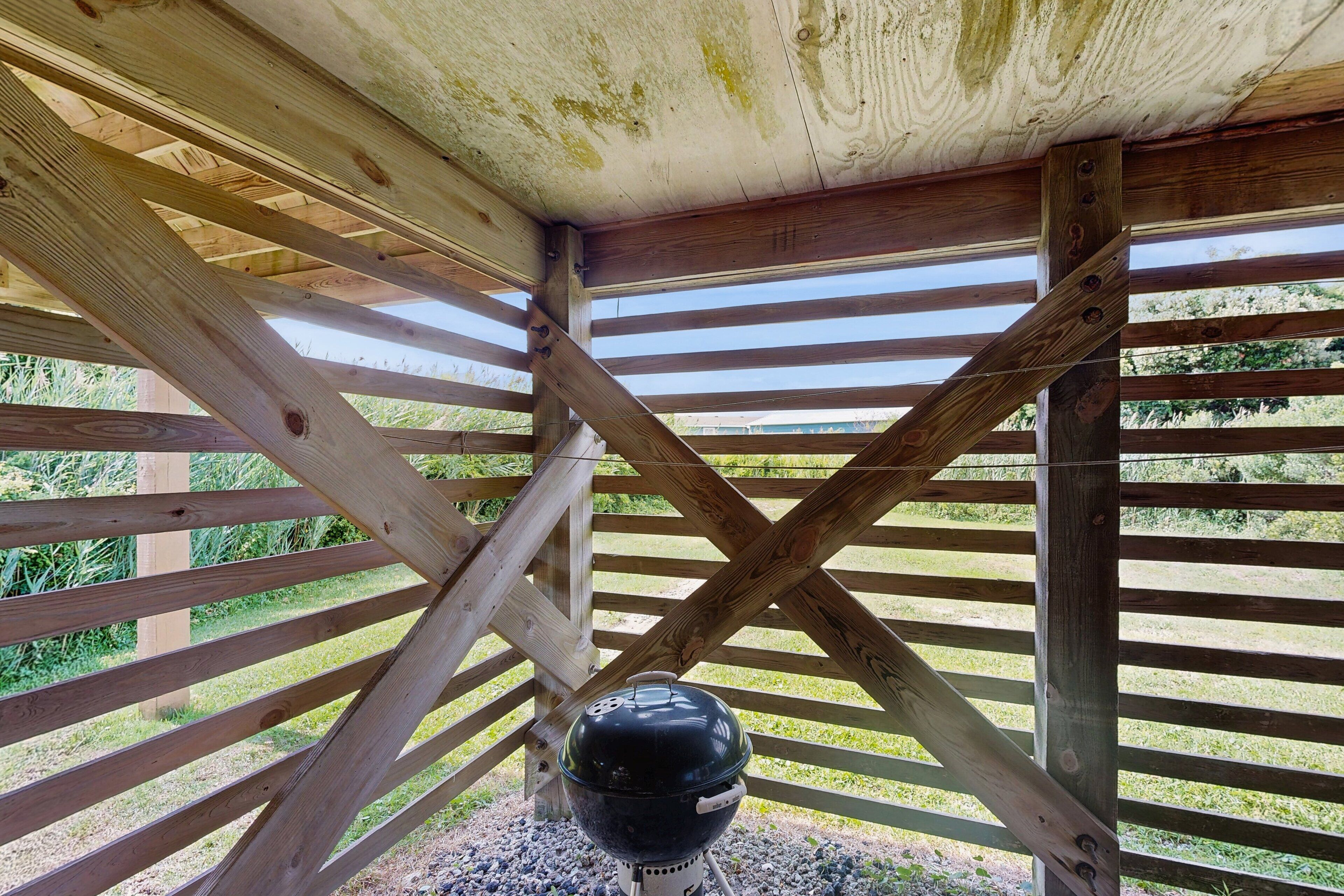 A wooden structure with a grill under a slatted roof.