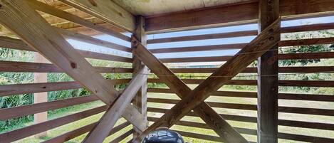 A wooden structure with a grill under a slatted roof.