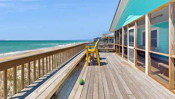 Ein Holzdeck mit Blick auf den Ozean, ein Stuhl und ein Gebäude mit großen Fenstern.