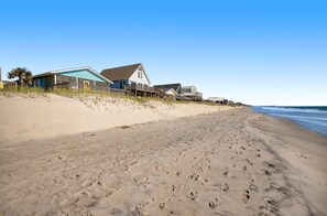A beachfront property with a sandy beach, a wooden staircase leading to a house, and a clear blue sky.
