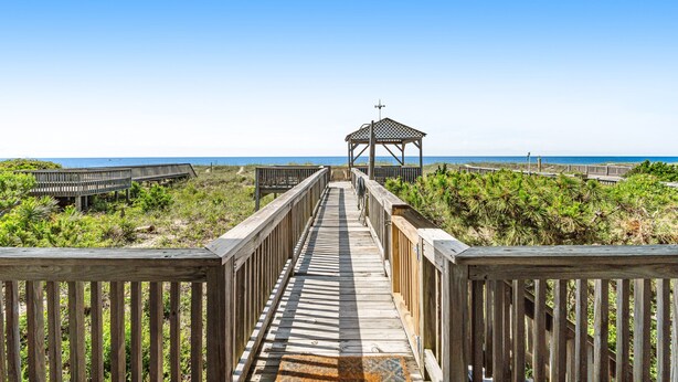 A wooden boardwalk leading to a gazebo with a view of the beach and ocean.