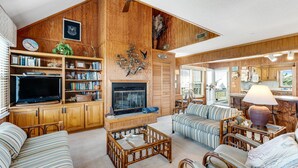 A spacious living room with a fireplace, wooden paneling, a television, and multiple seating areas.