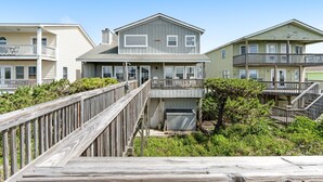 A beachfront property with a wooden deck, a covered outdoor seating area, and a two-story building with a balcony.