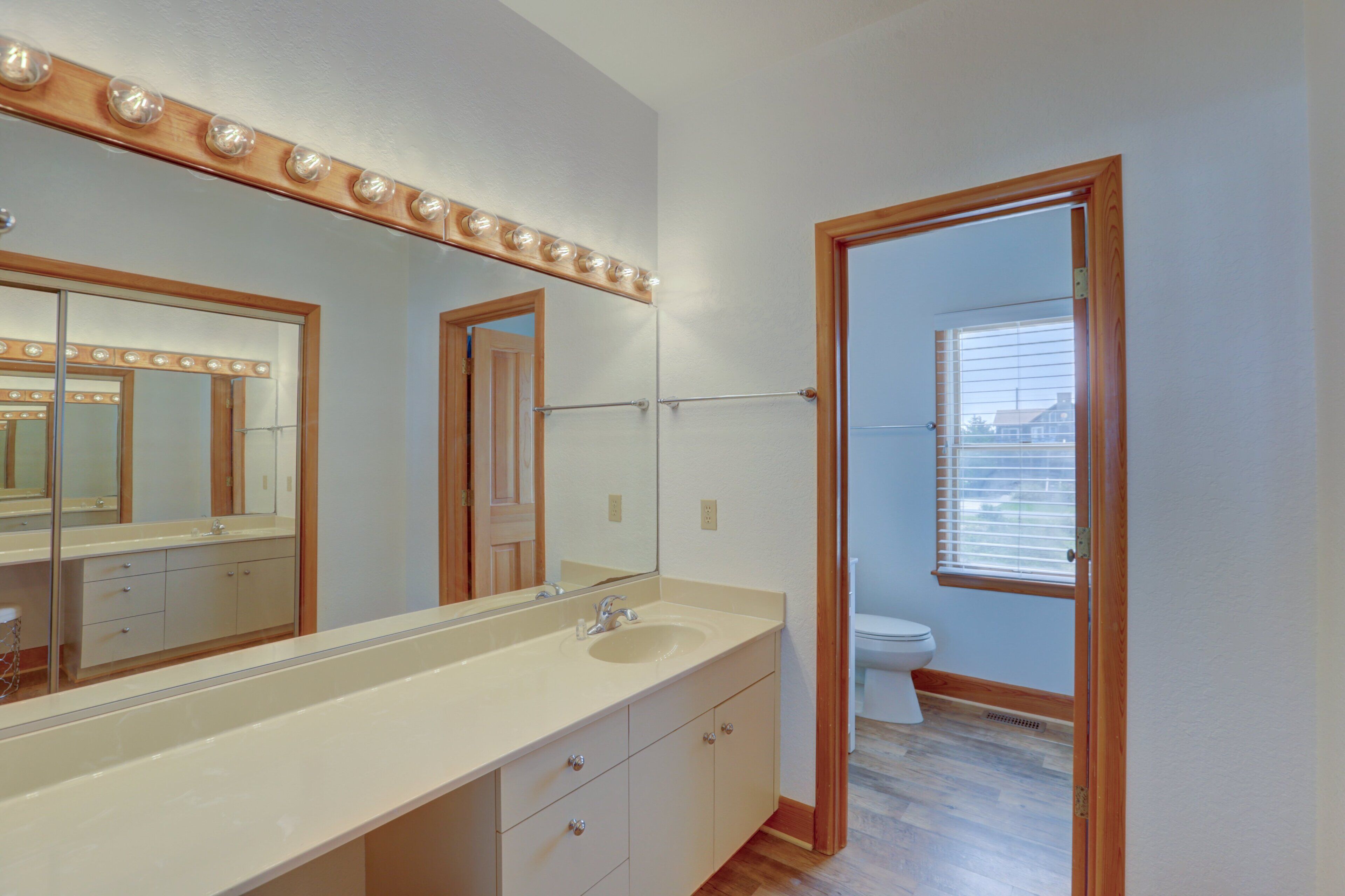 Une salle de bain avec un grand miroir, un meuble-lavabo et une fenêtre.